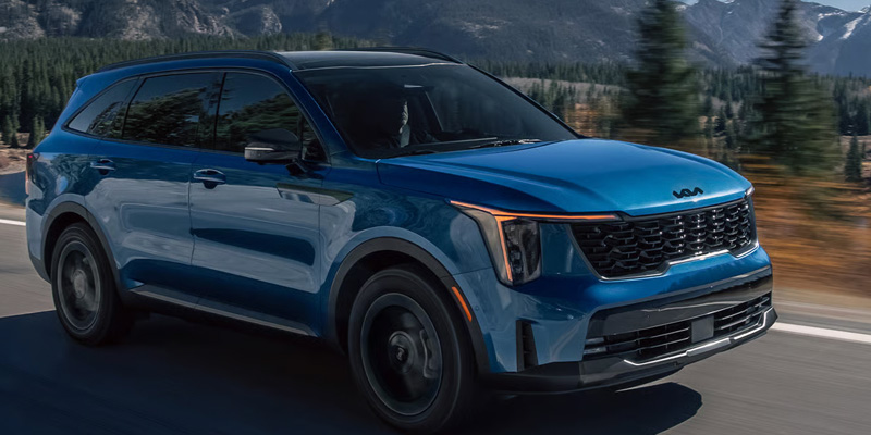 A blue Kia Sorento Hybrid driving on a scenic road with mountainous terrain in the background, showcasing its sleek and modern design.